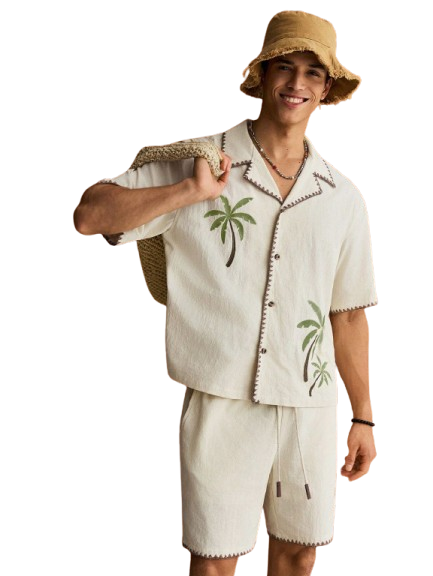 Person wearing a bucket hat and palm tree print shirt making a peace sign gesture.